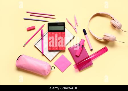 Modern calculator with headphones and different stationery on pale yellow background Stock Photo