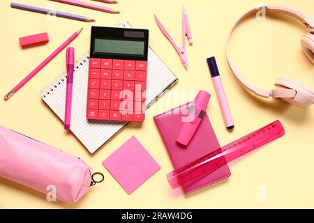 Modern calculator with headphones and different stationery on pale yellow background Stock Photo
