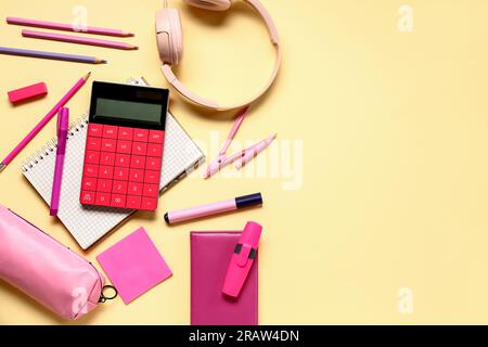Modern calculator with headphones and different stationery on pale yellow background Stock Photo