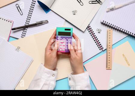 Woman with different stationery using calculator on blue background Stock Photo