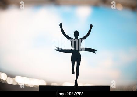 Crossing Boundaries: Runner's Silhouette Breaks the Finish Line Tape at Modern Athletics Stadium. Edit Space, Track and Field Competition Photo. Stock Photo
