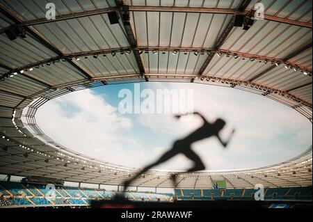 Unleashing Speed: Silhouette of an Athlete, Poised and Focused, Embracing the Twilight Glow at a Modern Sports Stadium. Stock Photo