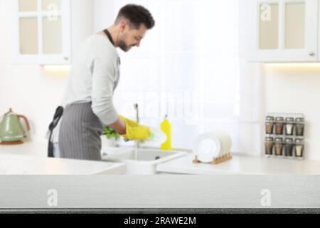 Man doing washing up in kitchen, focus on empty grey stone table Stock Photo