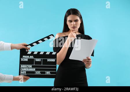 Actress performing role while second assistant camera holding clapperboard on light blue background. Film industry Stock Photo