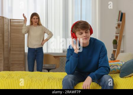 Teenage son listening music in headphones or playing online games ignoring  his mother Stock Photo - Alamy