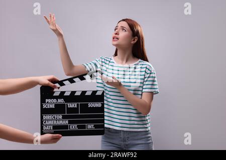 Emotional actress performing role while second assistant camera holding clapperboard on grey background Stock Photo