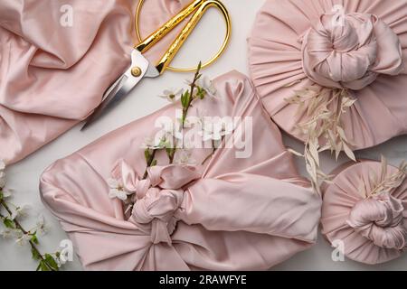 Furoshiki technique. Gifts packed in pink fabric and scissors on white table, flat lay Stock Photo