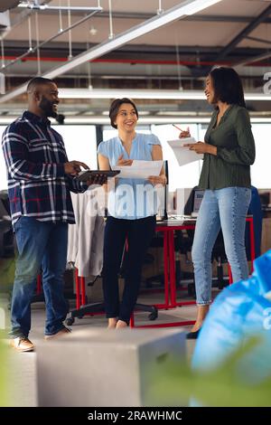 Diverse business people having meeting, discussing work and using tablet at office. Casual business, teamwork, communication and work, unaltered. Stock Photo