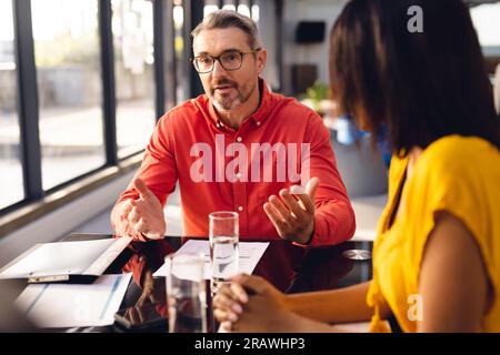 Diverse business people sitting at table, having meeting and discussing work at office. Casual business, teamwork, communication and work, unaltered. Stock Photo