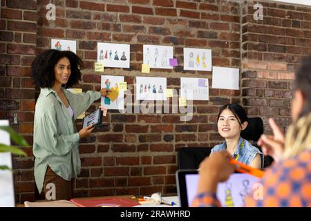 Happy diverse fashion designers using tablet and laptop, discussing designs in studio. Business, teamwork, communication, meeting, brainstorming, fash Stock Photo