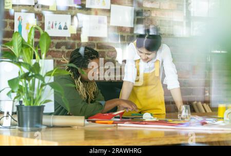 Busy diverse fashion designers discussing design project at desk in studio. Business, teamwork, fashion and design, unaltered. Stock Photo