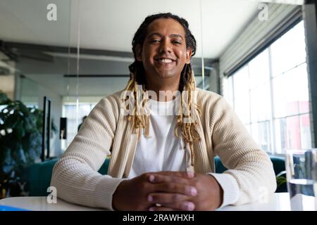 Happy biracial casual businessman sitting at desk in office having video call and smiling. Work, business, communication and casual office, unaltered. Stock Photo