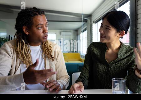 Two diverse casual business colleagues sitting at desk in discussion, having video call in office. Teamwork, work, business, communication and casual Stock Photo
