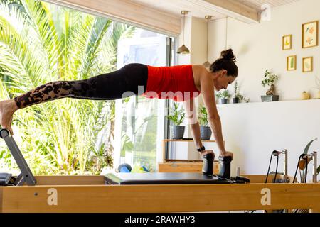 Focused caucasian female coach using reformer in pilates class. Exercise, wellbeing and healthy lifestyle, unaltered. Stock Photo