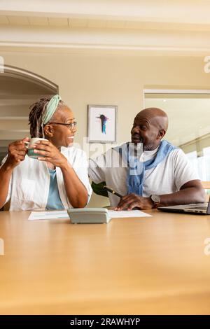 Happy senior african american couple having coffee using laptop and paying bills at home, copy space. Senior lifestyle, finance, retirement and domest Stock Photo