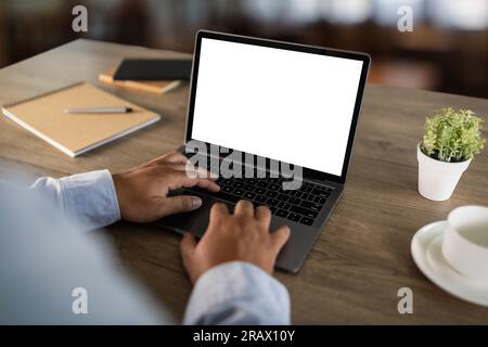 A young businessman is working on the laptop using a desktop computer with a blank screen and an empty copy space display. Stock Photo