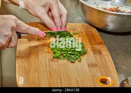 Chef cuts basil leaves on wooden cutting board with knife to add to the dish. Stock Photo