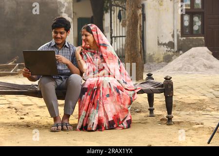 Happy rural Indian family in village Aspirational family sitting with a bank manager who is showing a laptop screen to the family . Stock Photo