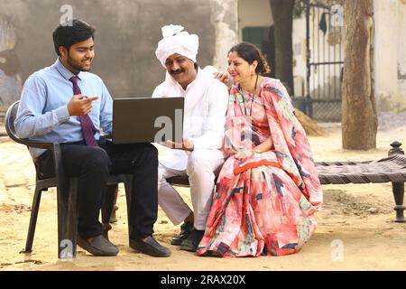 Happy rural Indian family in village Aspirational family sitting with a bank manager who is showing a laptop screen to the family . Stock Photo