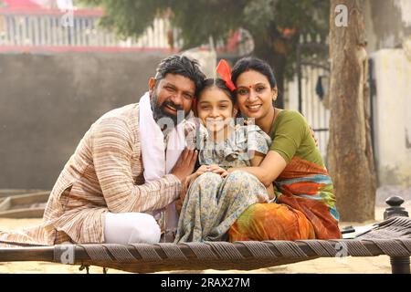Happy rural Indian family sitting together outside their cottage in day time smiling while looking at the camera Stock Photo