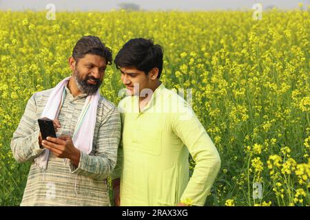 Happy rural Indian men standing in a mustard field taking a selfie from their phone Stock Photo