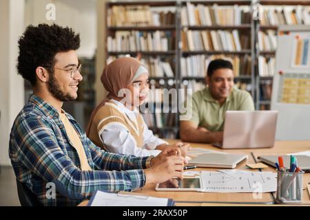 Migrant students studying foreign language while sitting together at table with computers and textbooks Stock Photo