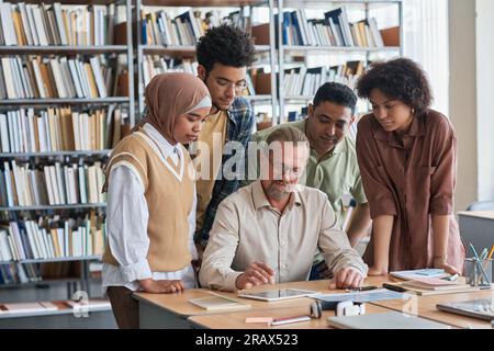 Group of students using tablet pc with teacher during lesson in the library Stock Photo