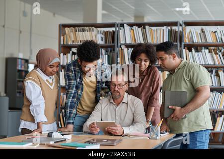 Teacher having lesson with migrant students, they watching presentation on digital tablet during lesson Stock Photo