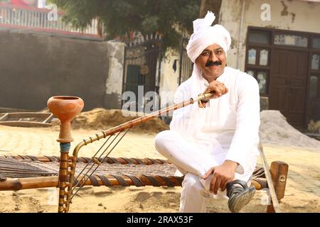 Happy Rural Indian Village man in turban sitting outdoors in a day time. Hookah in hand. Stock Photo