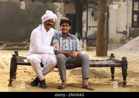 Happy and proud Indian Father sitting with his son on a cot looking into the camera. Stock Photo