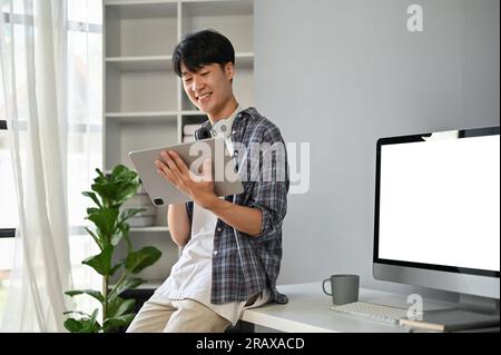 A smart and handsome young Asian male programmer or freelancer in a casual clothes using his digital tablet in the office. Stock Photo