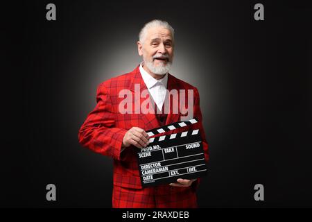 Senior actor with clapperboard on black background. Film industry Stock Photo