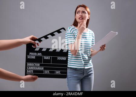 Emotional actress performing role while second assistant camera holding clapperboard on grey background, selective focus Stock Photo