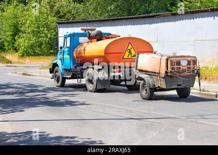 An old water tanker truck trailering a mobile construction compressor with a hanging pneumatic jackhammer on a sunny day. Copy space. Stock Photo