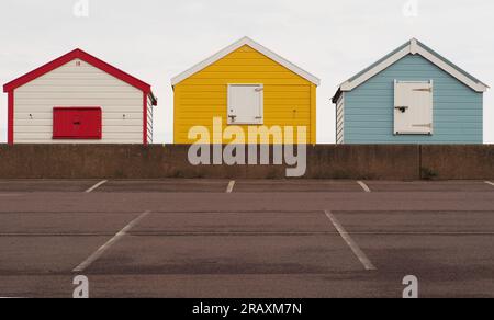 Three colourful beach huts at Southwold, Suffolk. UK with the carpark and low wall in the foreground Stock Photo