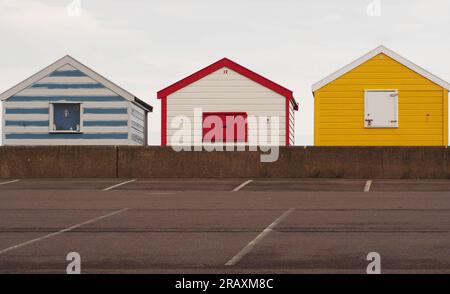 Three colourful beach huts at Southwold, Suffolk. UK with the carpark and low wall in the foreground Stock Photo