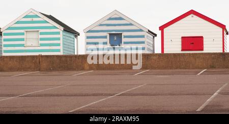 Three colourful beach huts at Southwold, Suffolk. UK with the carpark and low wall in the foreground Stock Photo