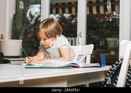 Cute little boy doing homework for school, writing in excersice notebook Stock Photo