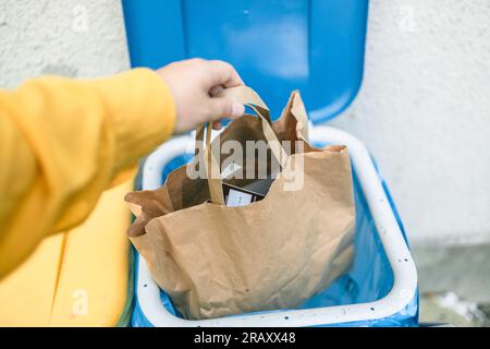 Full size of caucasian woman sorting garbage, throwing a used paper bag in a small recycle bin at outdoor near a home  Stock Photo