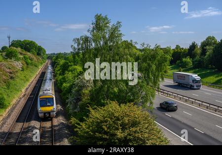 Train travelling along track running parallel with the M40 motorway, Warwickshire, England. Stock Photo