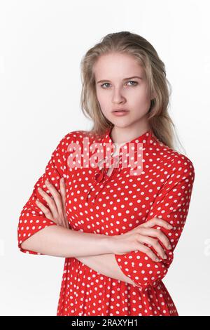 Portrait of serious young woman has her arms crossed over chest looking at camera. Ignoring Caucasian female 21 years old dressed in summer red dress Stock Photo