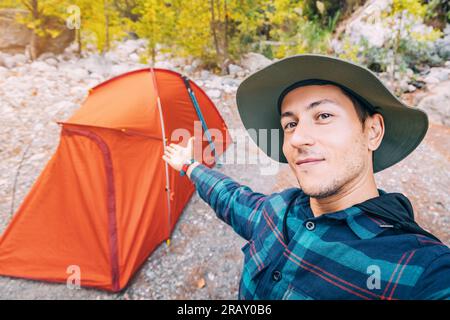 Happy man traveler naturalist against the backdrop of a camping tent and picnic spot in the woods Stock Photo