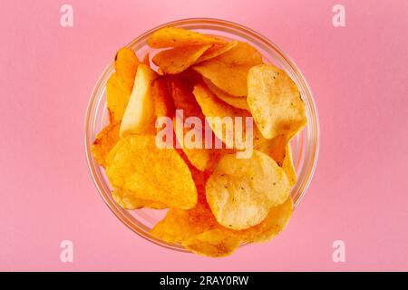 Potato chips in glass bowl isolated on pastel pink background. Top view Stock Photo