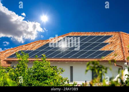 Solar panels on tiled roof on cottage on blue sky with sun and sun reflection on black panels. Solar energy Sustainable Resources Stock Photo