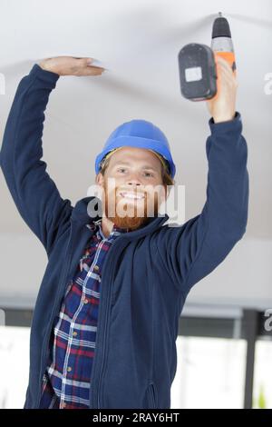 happy handyman using cordless drill to the ceiling Stock Photo