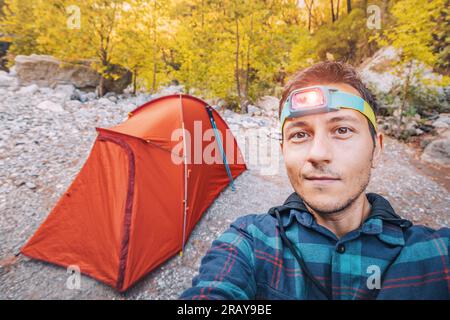 A hiker with a headlamp in the evening against the background of a tent during a trail travel Stock Photo