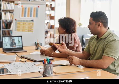 Migrant students having online lesson with teacher while sitting at table and studying foreign language Stock Photo