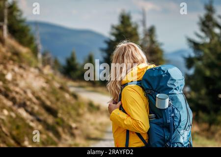 Woman hiking in mountain. Tourist with yellow jacket and backpack walks on trekking trail Stock Photo
