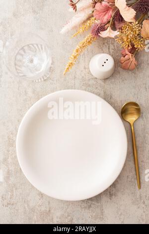 Table setting, plate and golden cutlery on a brown background, empty wine glass, top view of the served table decorated with dry flowers Stock Photo