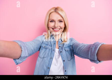 Closeup portrait of lovely aged senior lady beaming smiling making self photos wear denim shirt isolated pink color background Stock Photo